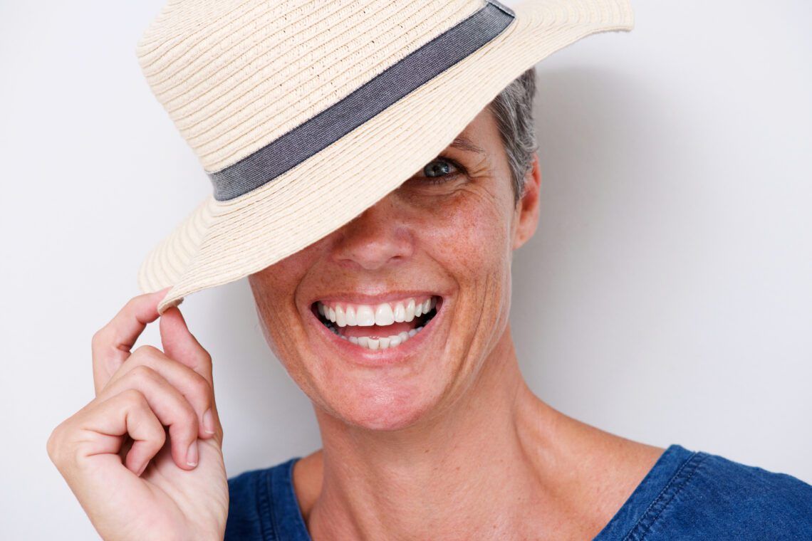 close up happy older woman laughing with hat UB85FRR scaled